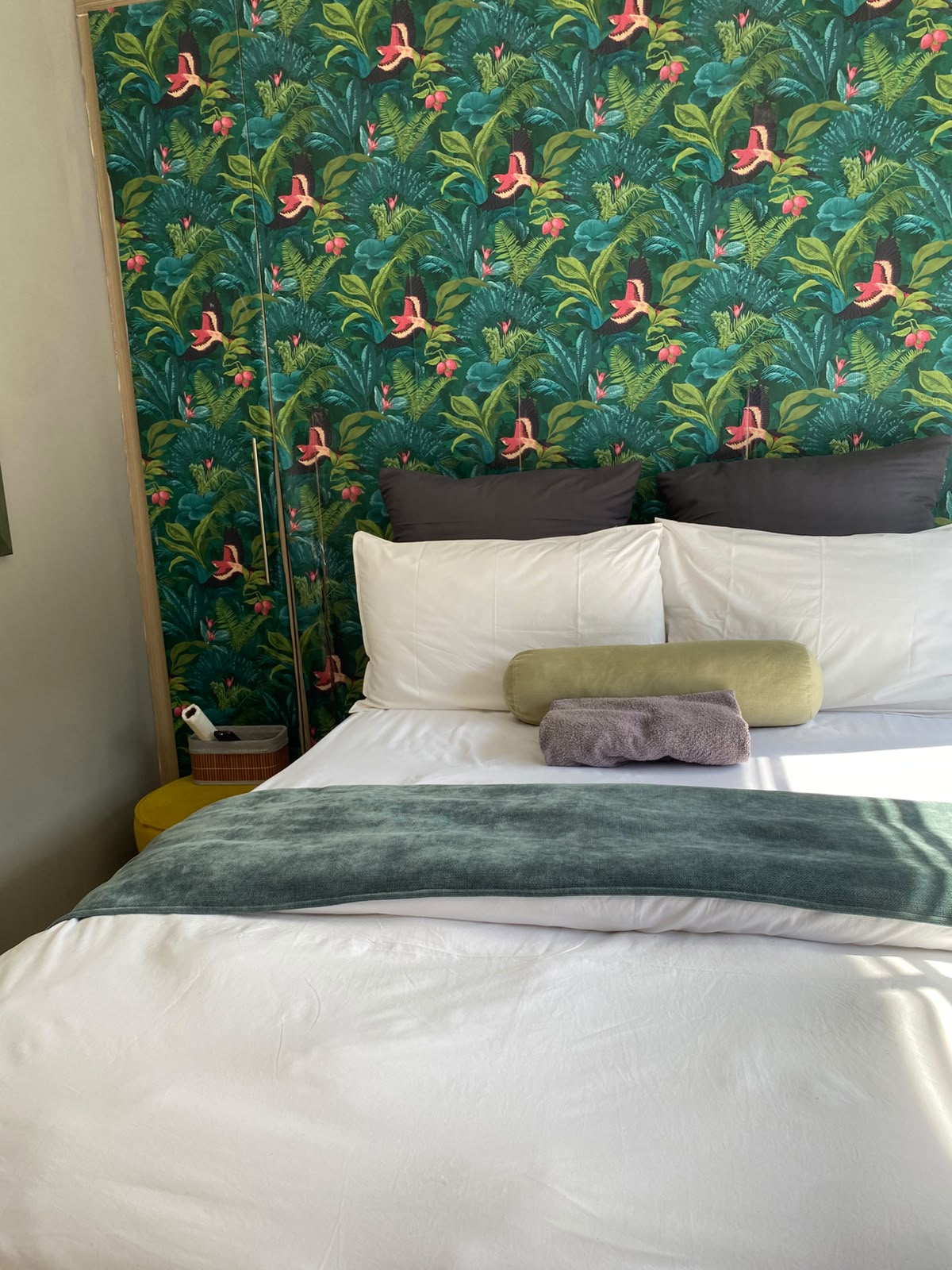 Room 5 bed with tropical bird wallpaper, green bolster and fresh towels
